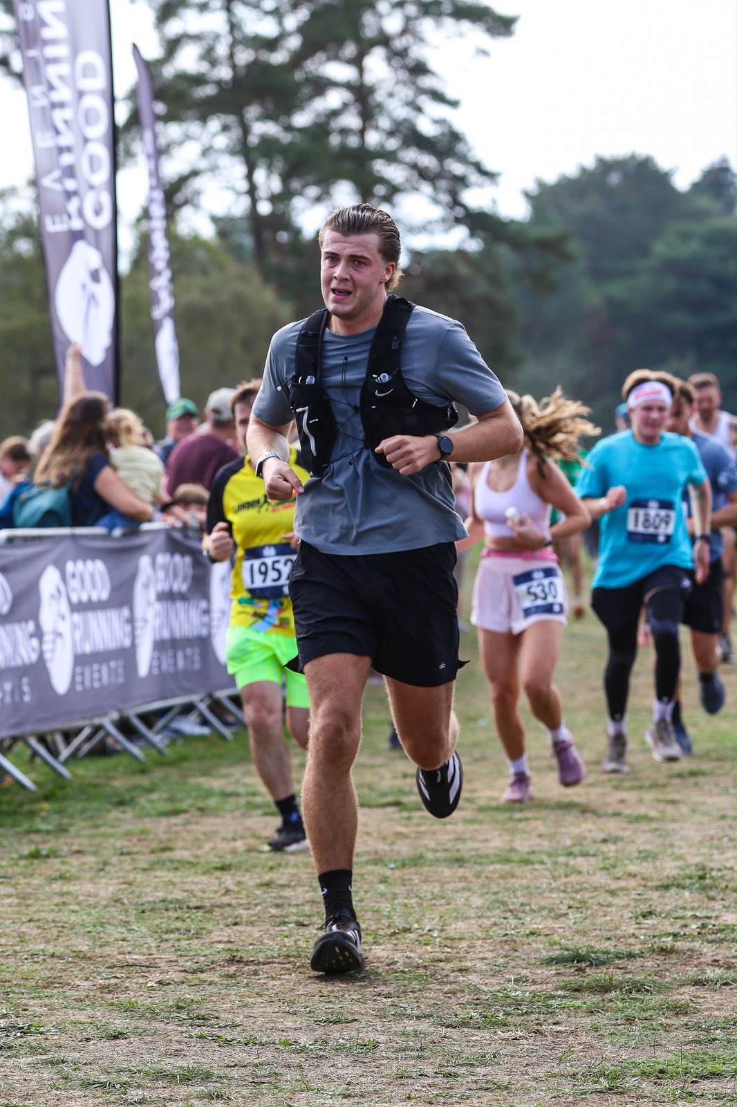 Luke running towards the finish of the half marathon with spectators and a Good Running banner behind him
