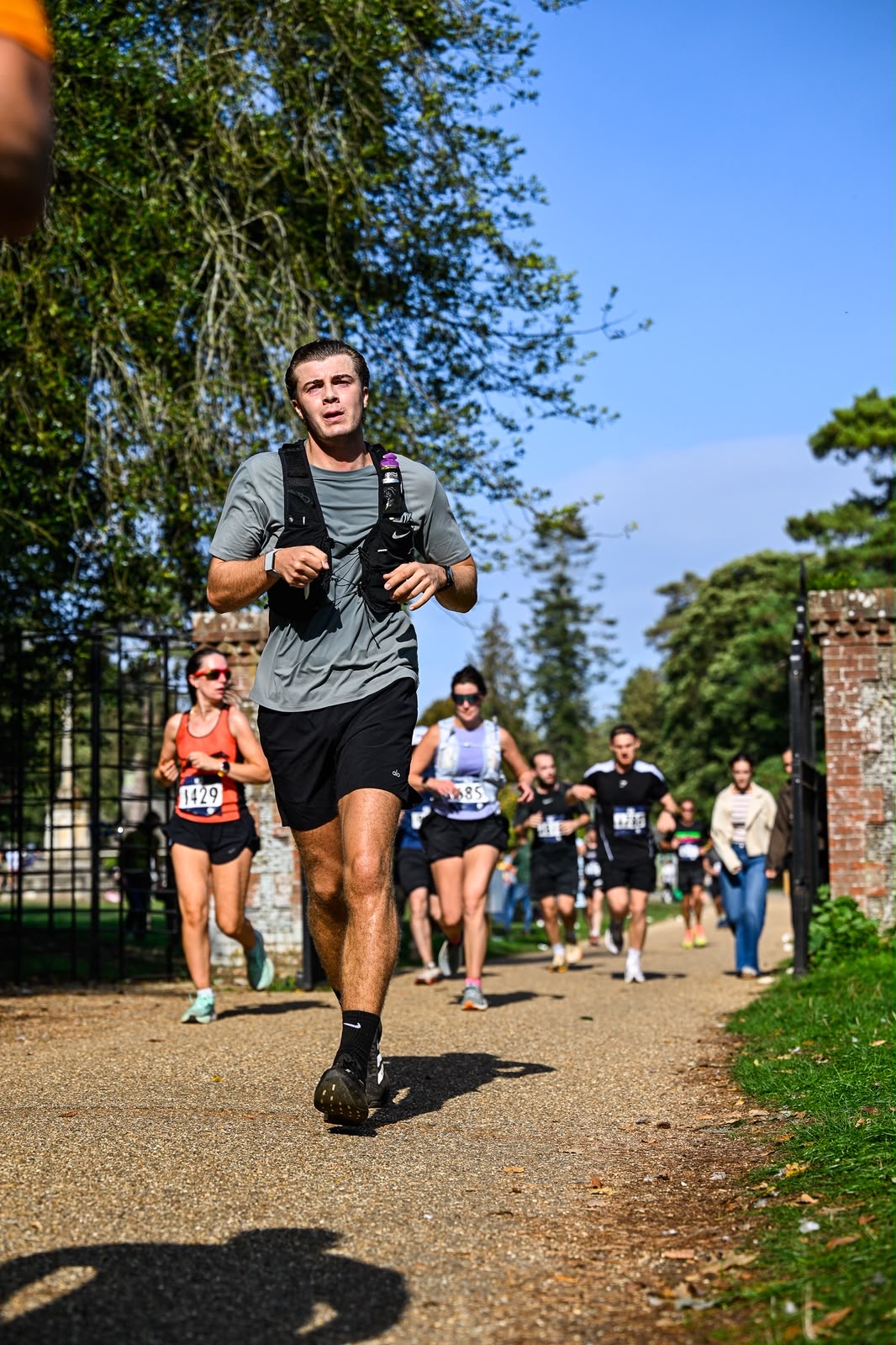 Luke running along a gravel track through the estate gates with other runners behind him