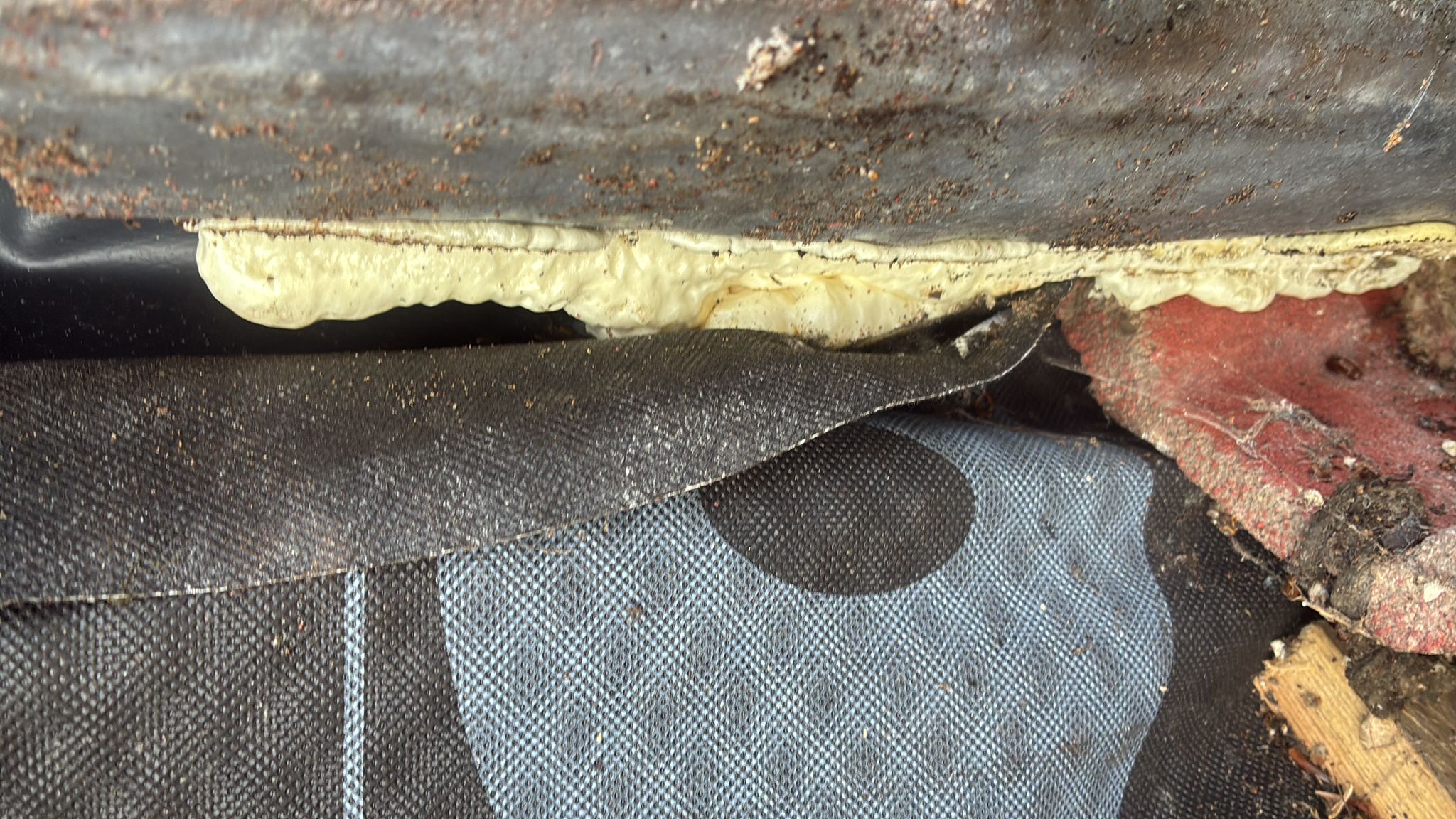 Deteriorated expanding foam and damaged materials beneath the peeled-back roof membrane at a chimney repair in Roughton