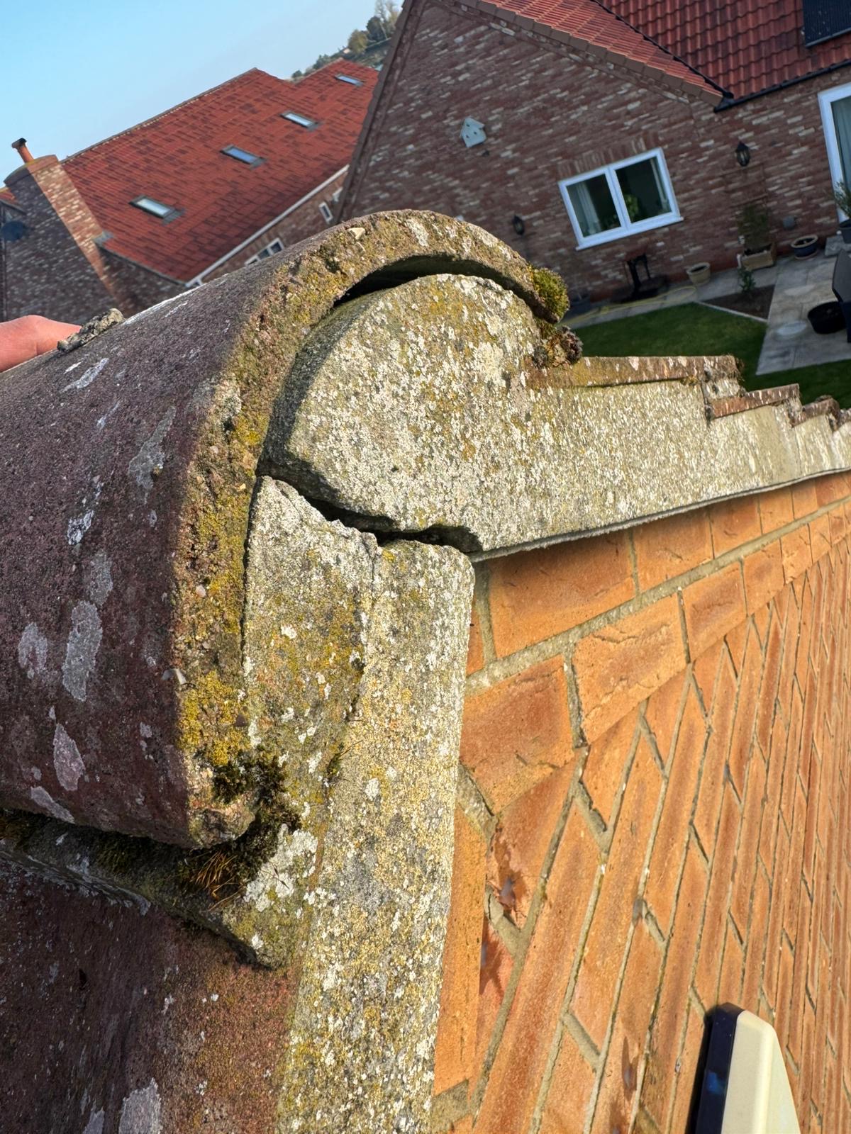 Heavy lichen and moss covering a ridge end cap with visible deterioration on a roof in Wisbech