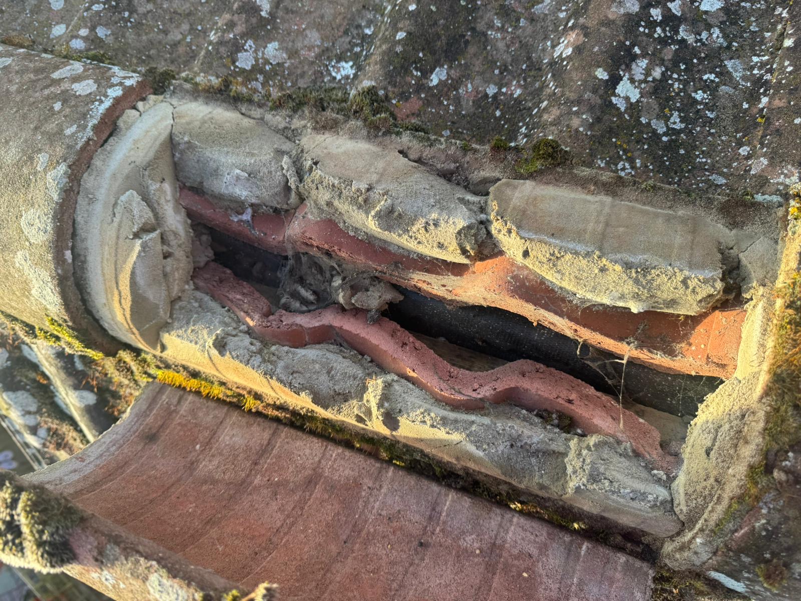 Multiple layers of old crumbling mortar and deteriorated tiles exposed during a roof clean in Wisbech