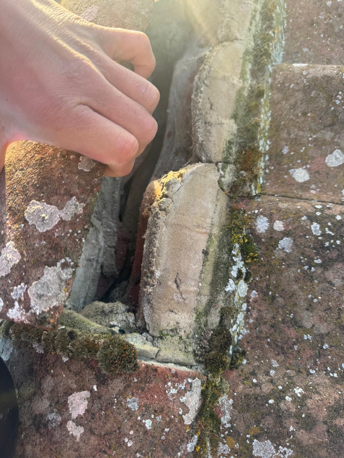 Hand lifting a ridge tile to reveal crumbling mortar on a roof in Wisbech, Cambridgeshire