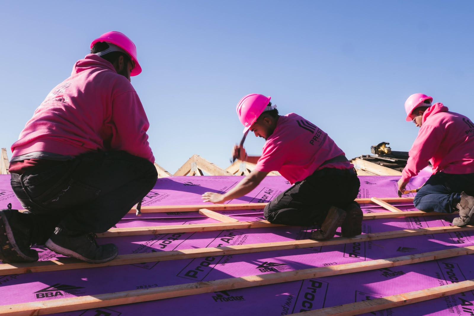 The Prestige Roof team in pink hard hats and hoodies battening the roof under a blue sky