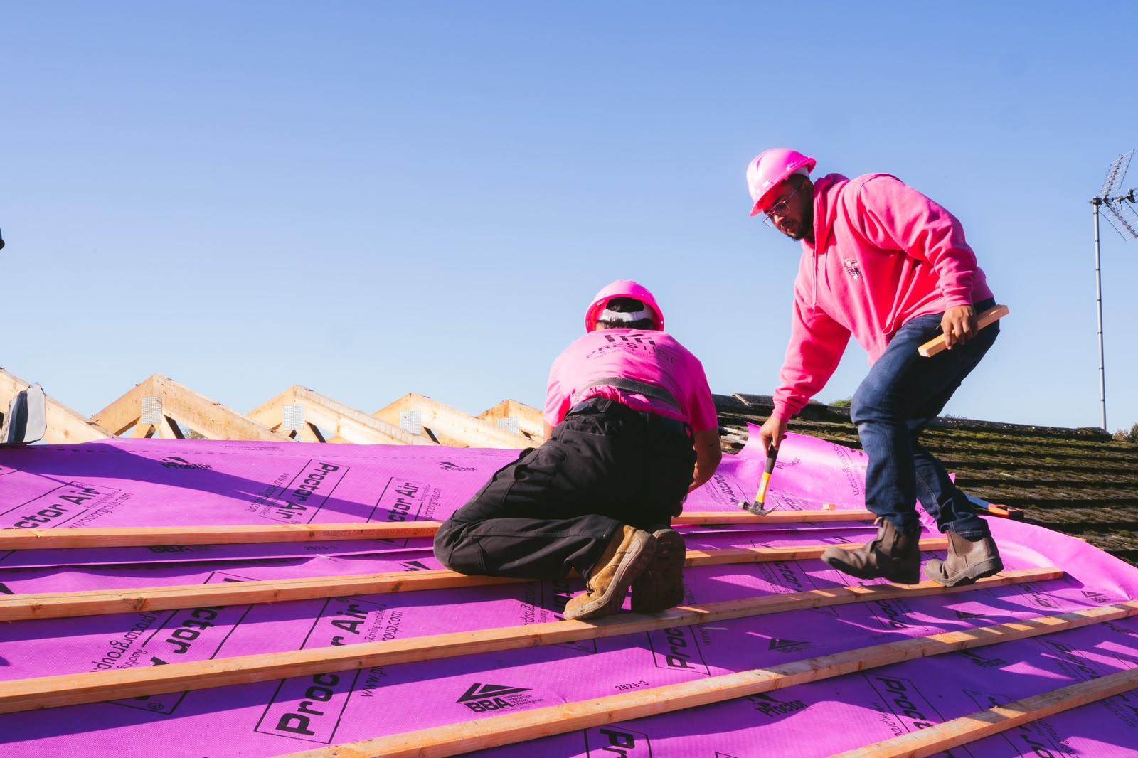 Two roofers in pink hard hats fixing treated battens on the new breathable membrane