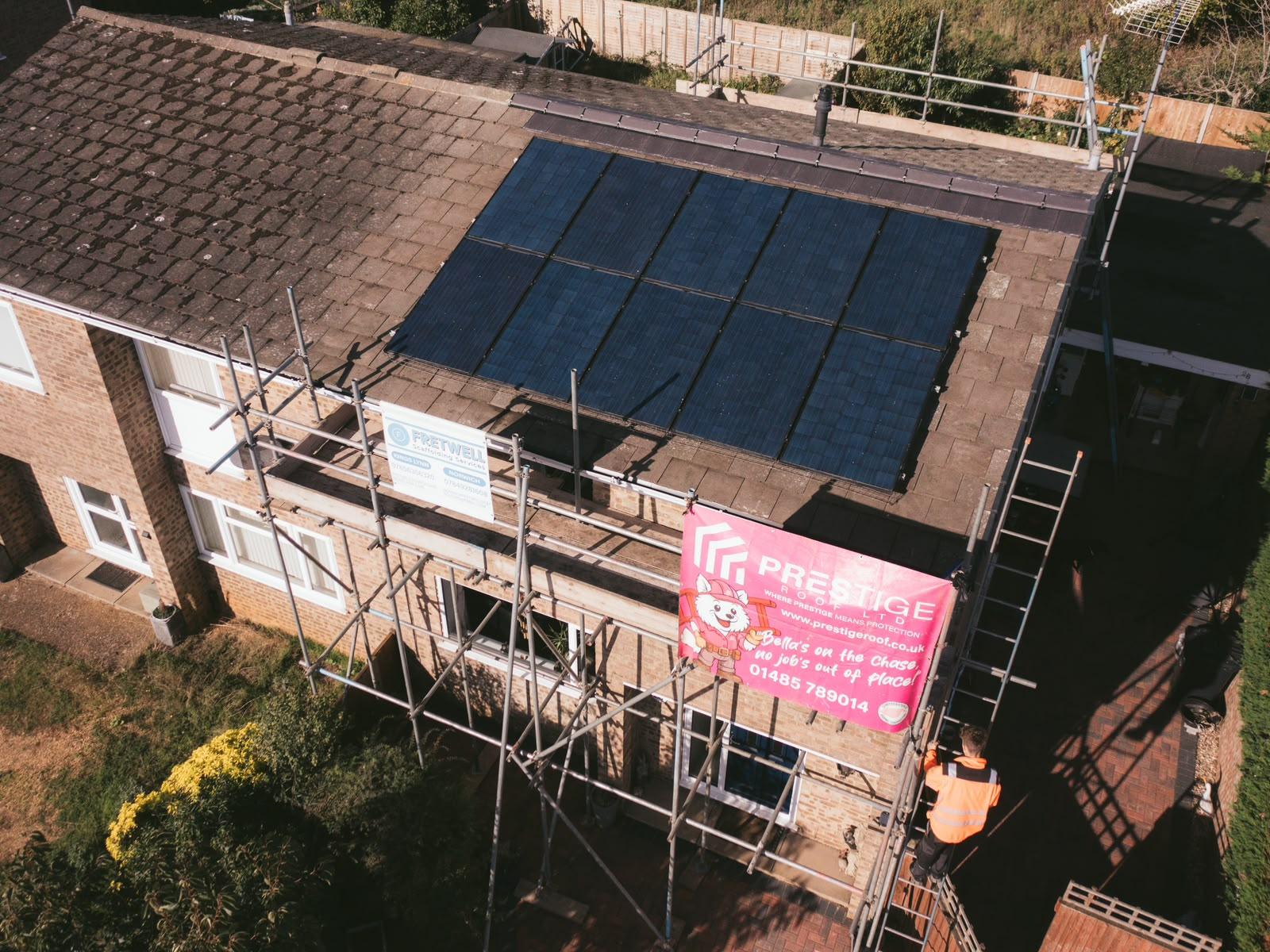 Scaffold around the house with a pink Prestige Roof banner, ready for the roof replacement