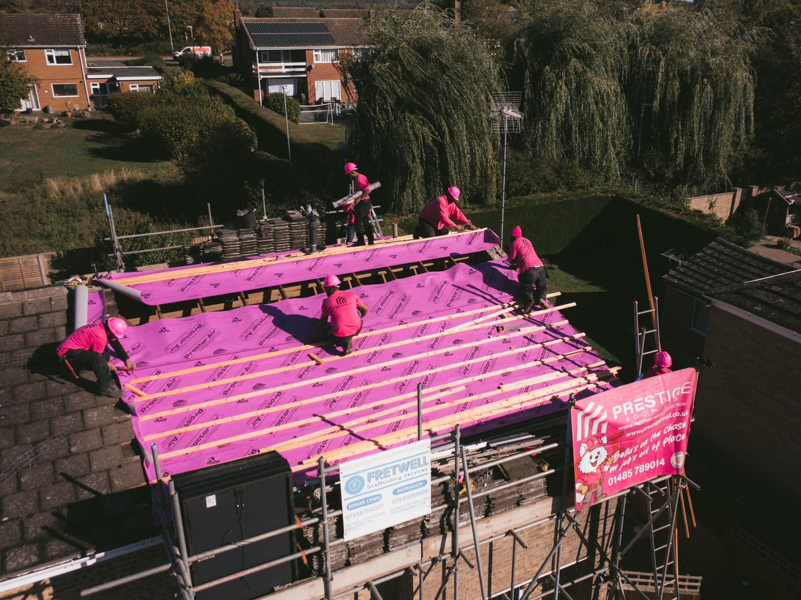 Drone shot of the Prestige Roof team in pink hard hats working across the new roof membrane and battens