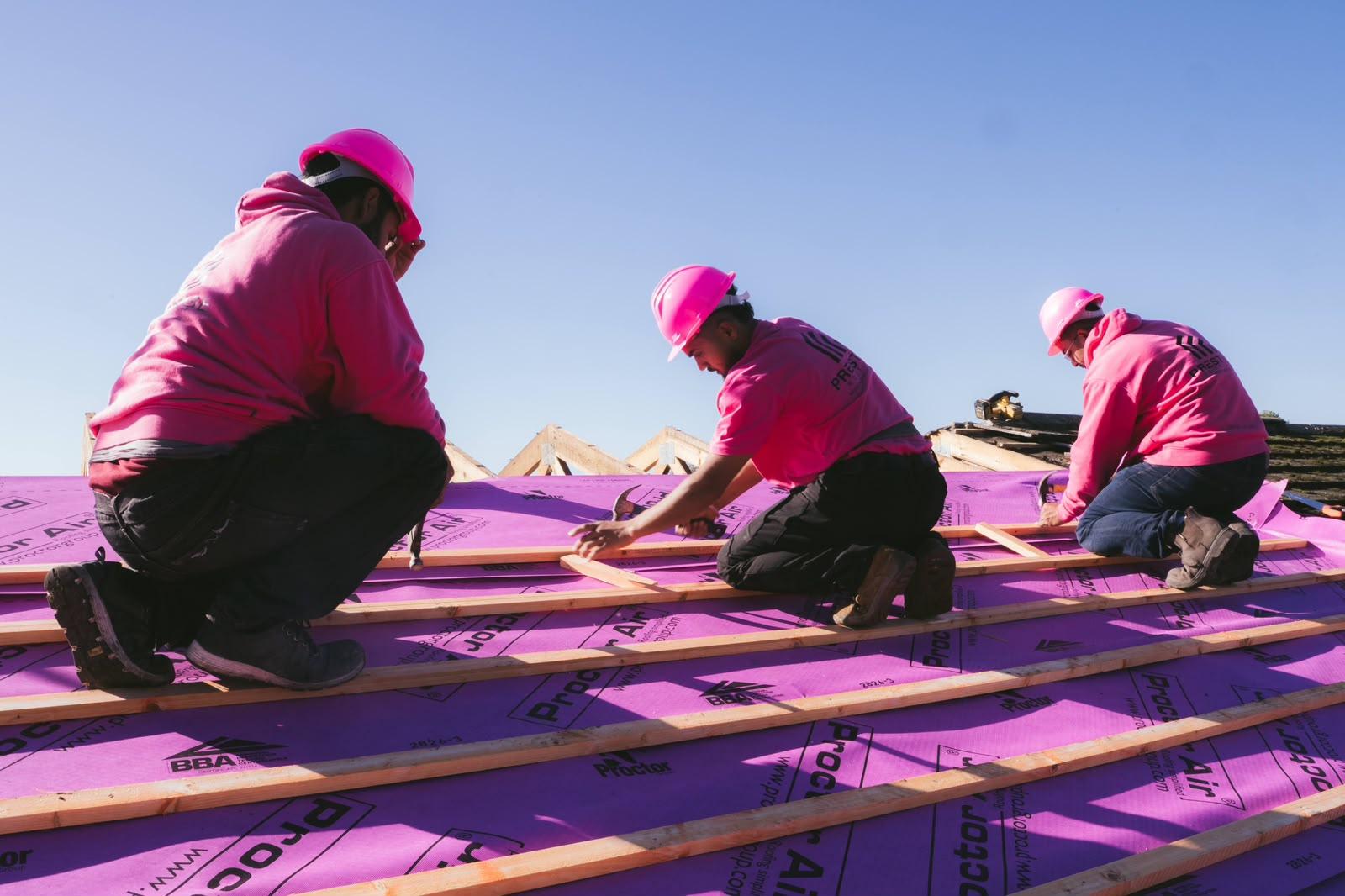 Three Prestige Roof roofers in pink hard hats kneeling on the roof fixing battens